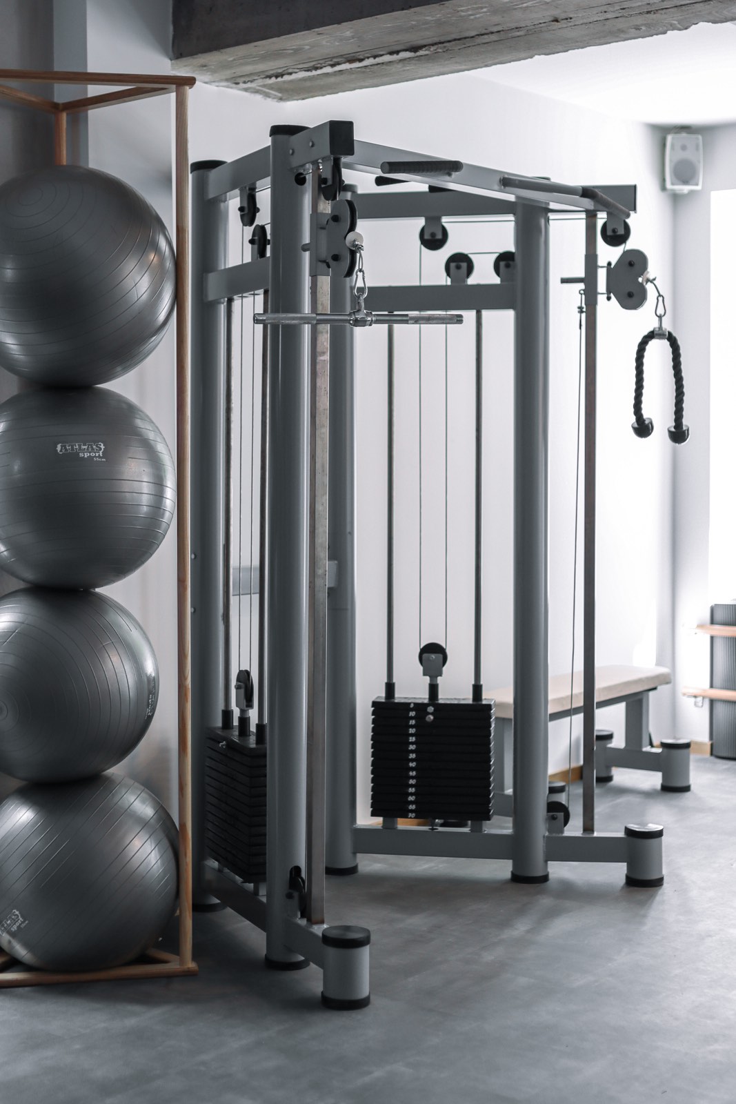 Kabl kros sprava u sivoj boji sa dva tega, prečkom za zgibove, lat šipkom i užetom za triceps u fitnes studiju