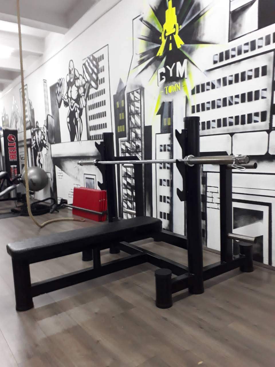 Ravni bench sa stalkom za šipku, kukama po visini i trnovima za tegove, u teretani sa oslikanim zidom