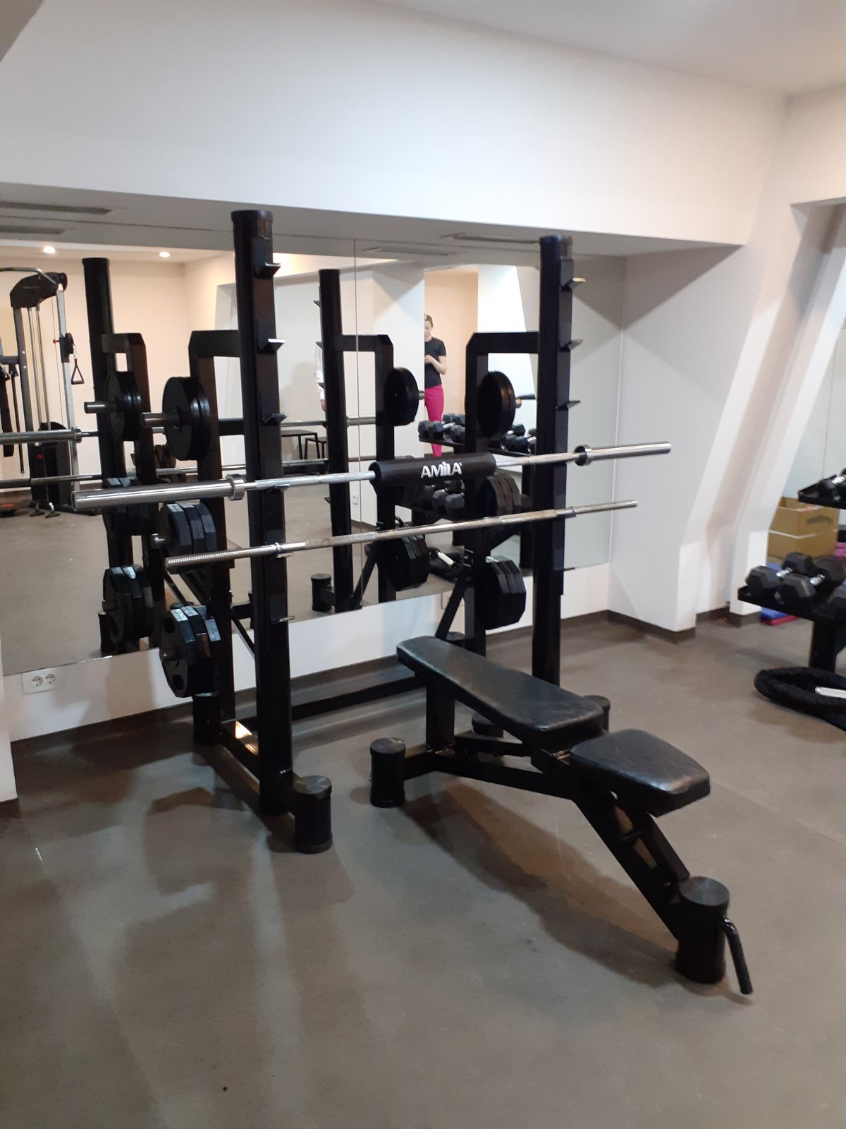 Stalak za bench sa dve šipke, mestima za odlaganje tegova i podesivom klupom, ispred ogledala u teretani