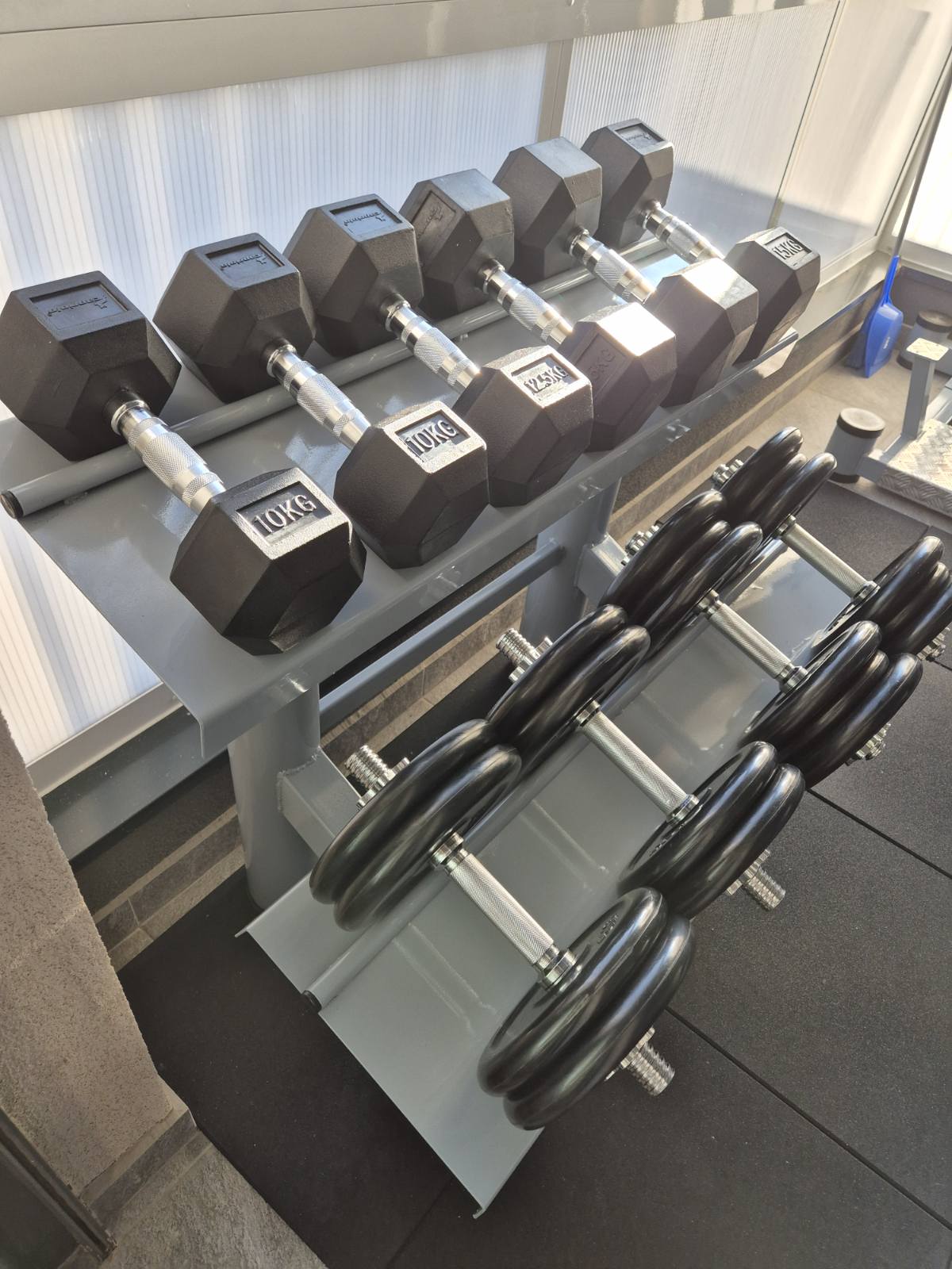 Stalak za bučice sa dva kosa nivoa odlaganja u sivoj boji, sa heksagonalnim bučicama od 10 i 15 kilograma